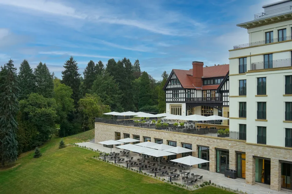 Hotel mit Terrassen und weißen Großschirmen vor bewaldetem Hang